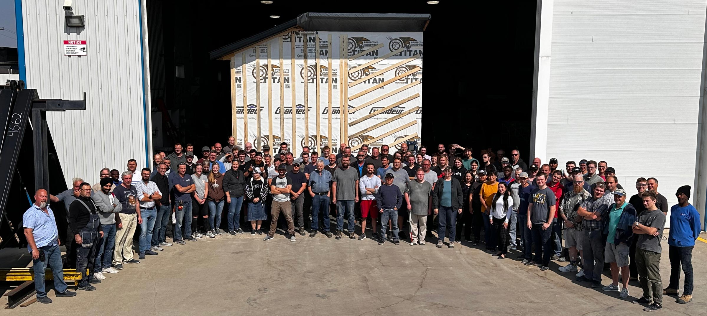 large group of staff outside the entrance to the Grandeur workshop, standing in front of a finished modular home section.