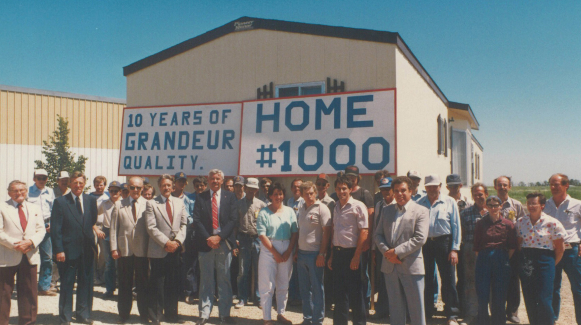 a crowd of mostly male workers outside, standing in front of a large mobile home with a sign reading "home #1000"